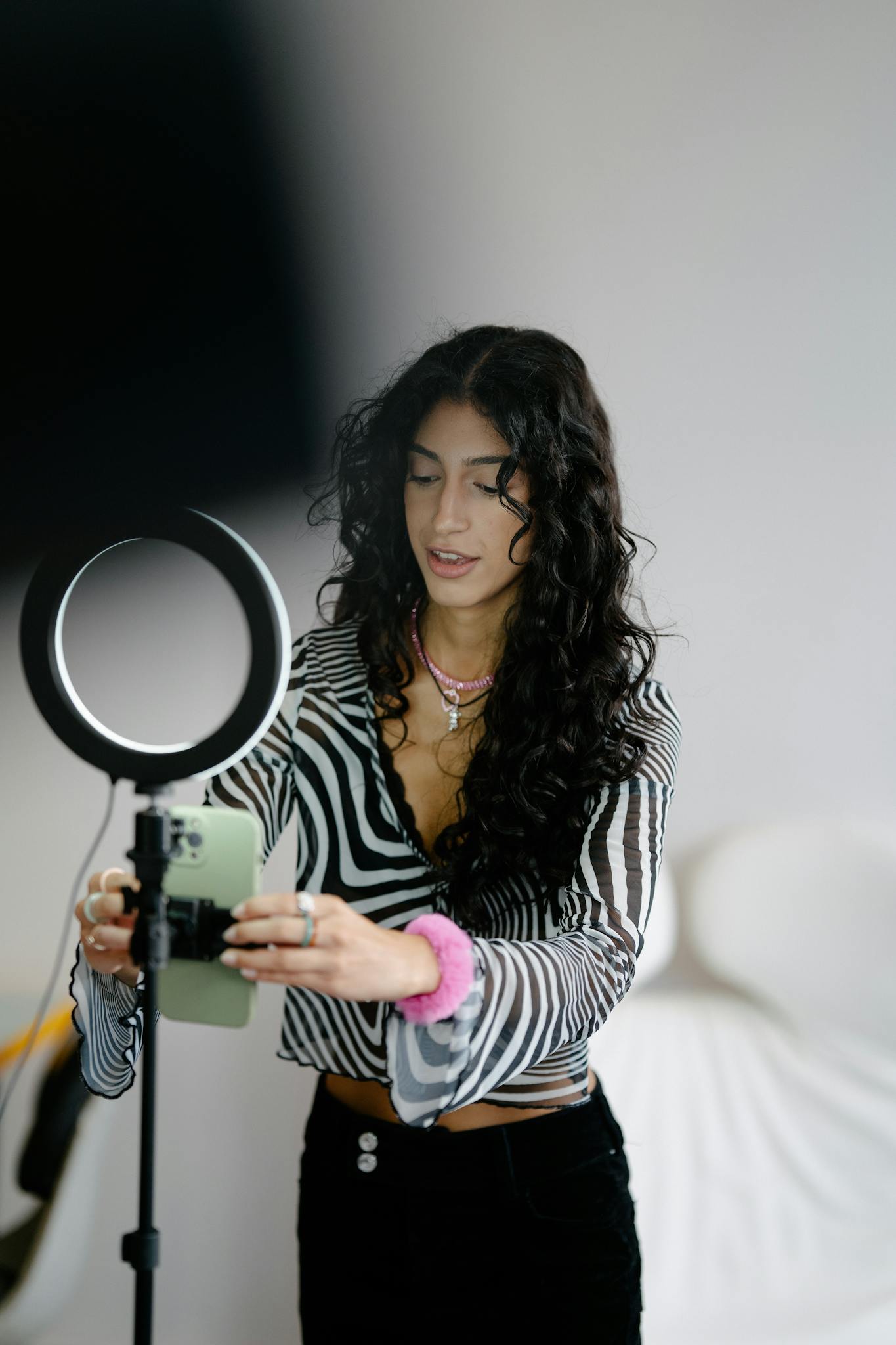 A woman adjusts a smartphone with a ring light in a studio setup, preparing for photography.